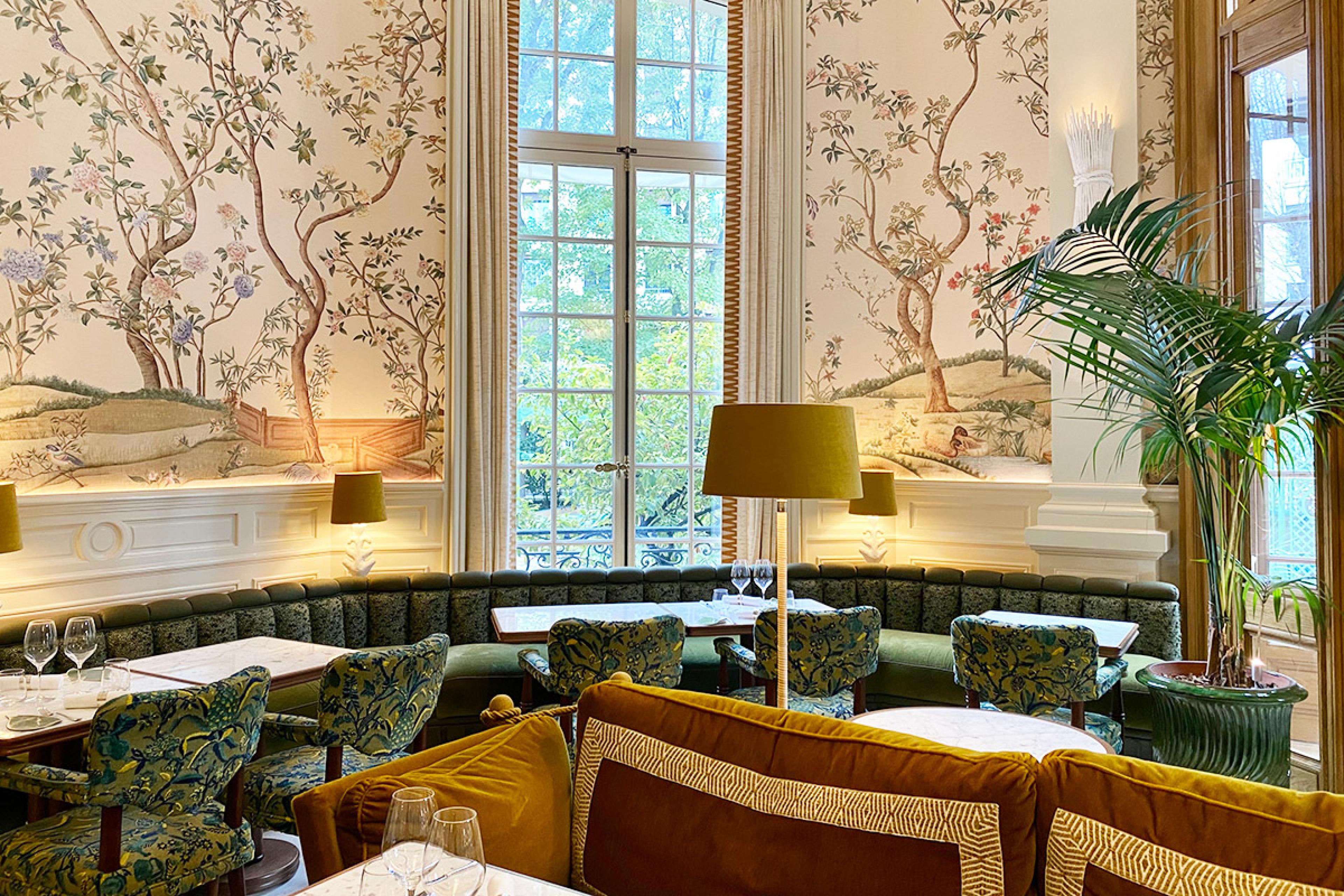 detail of a hotel dining area with green banquette seating and vine murals on a white wall