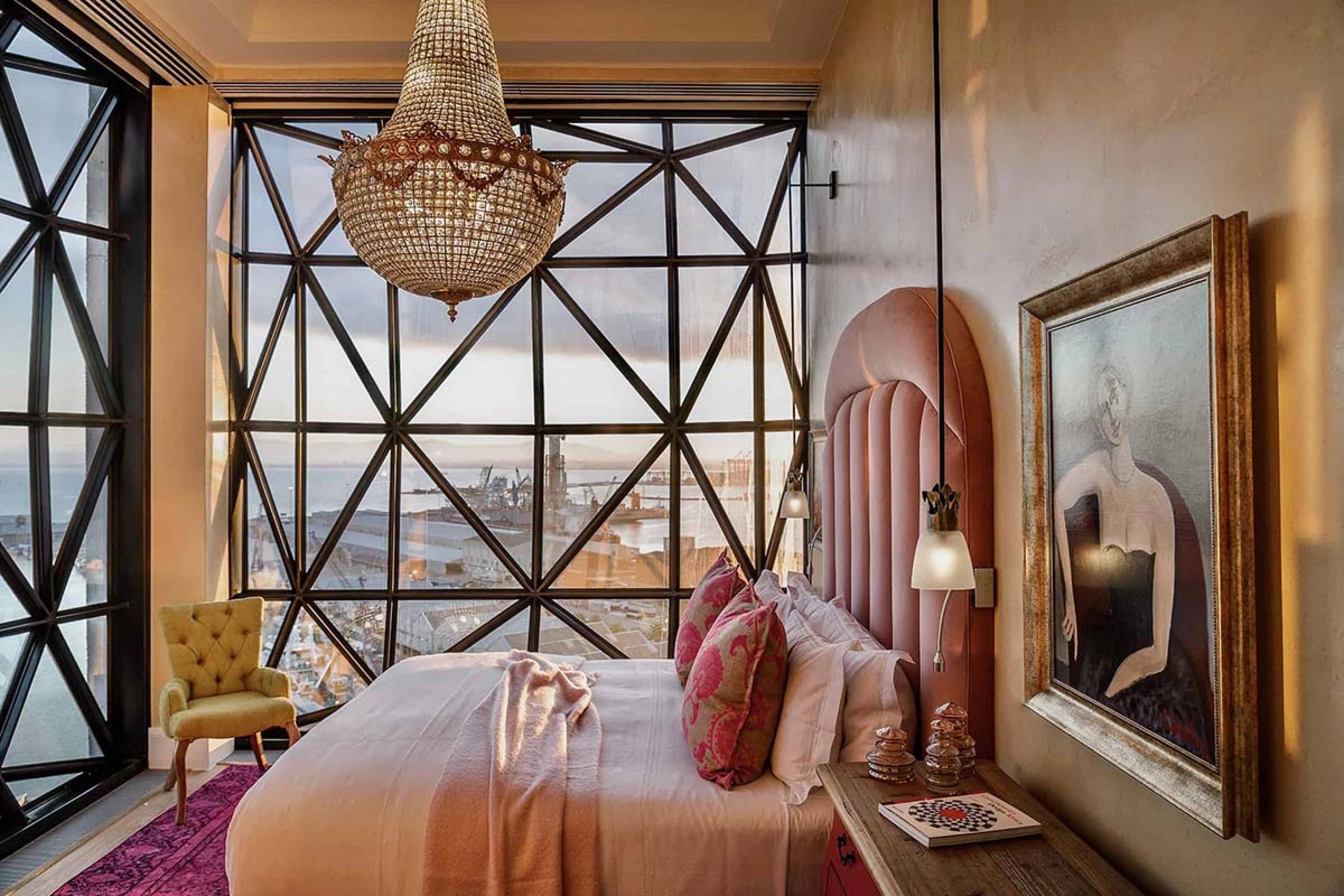 bed room with black framed geometric windows, a glass chandelier and a blush colored bed and headboard