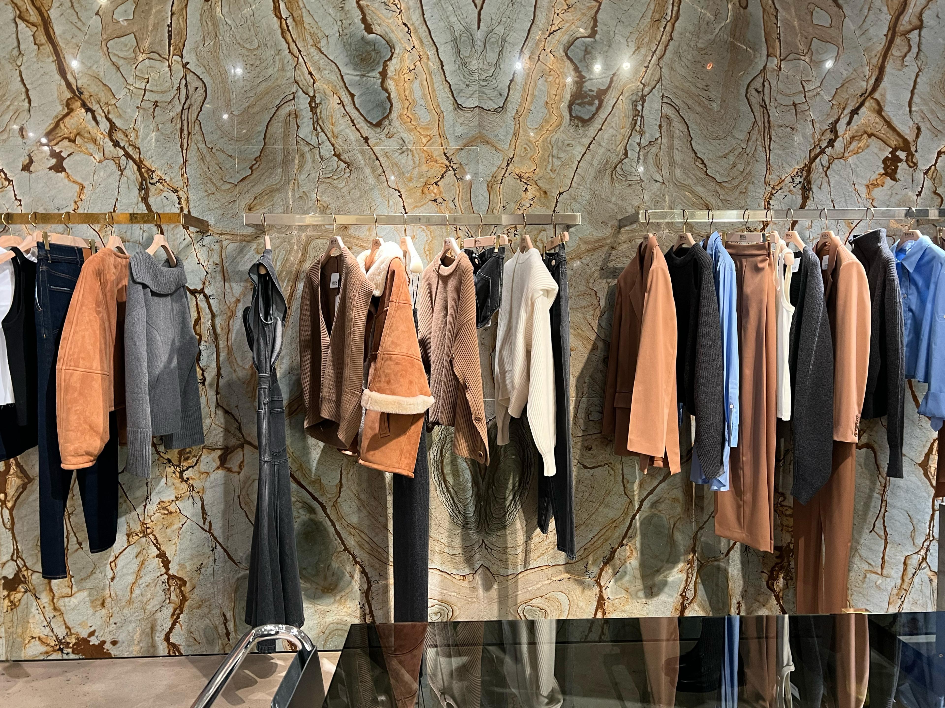 clothing rack with warm toned clothing in front of a marble patterned wall